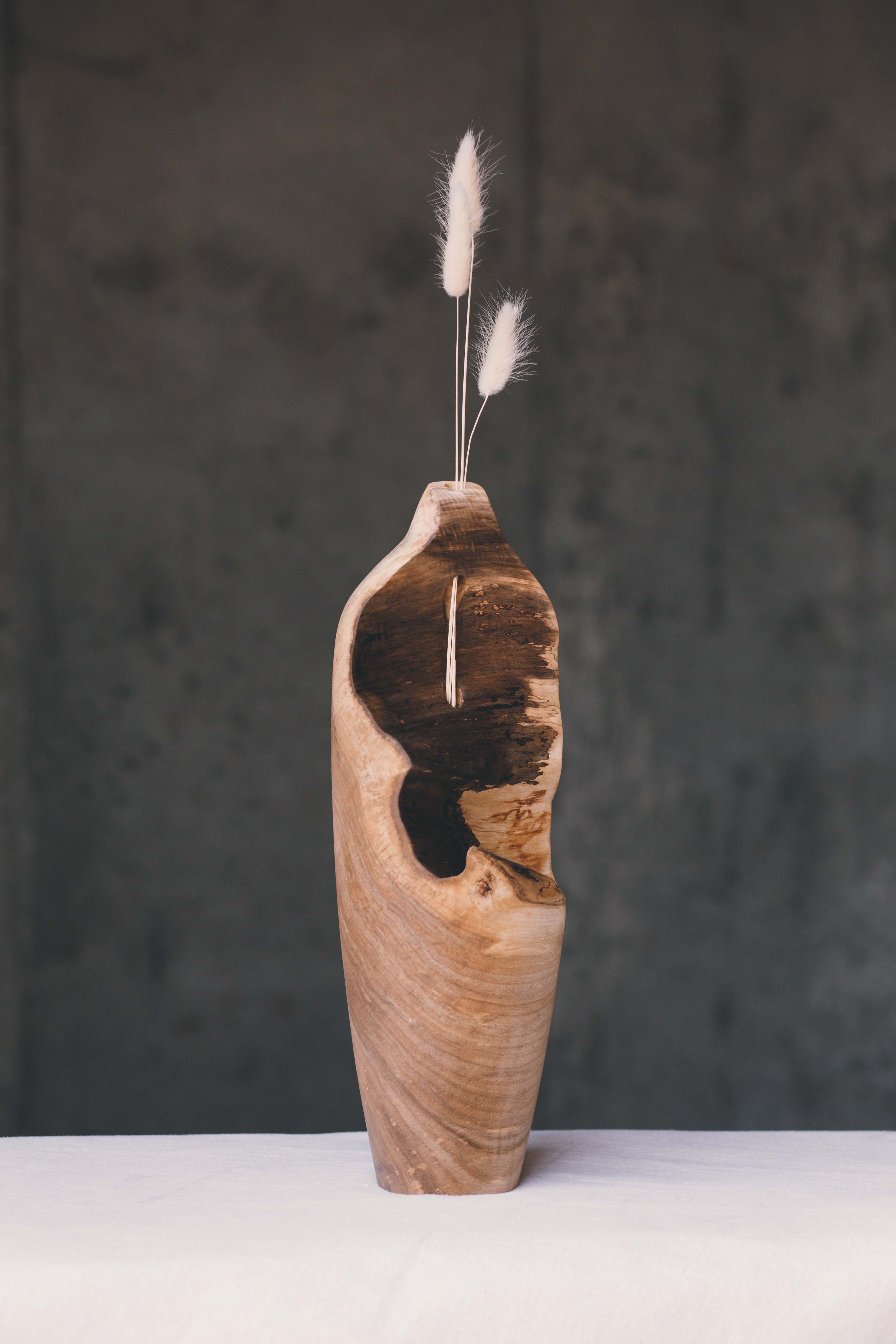 A tall wooden bud vase with exposed edge and dried flowers.