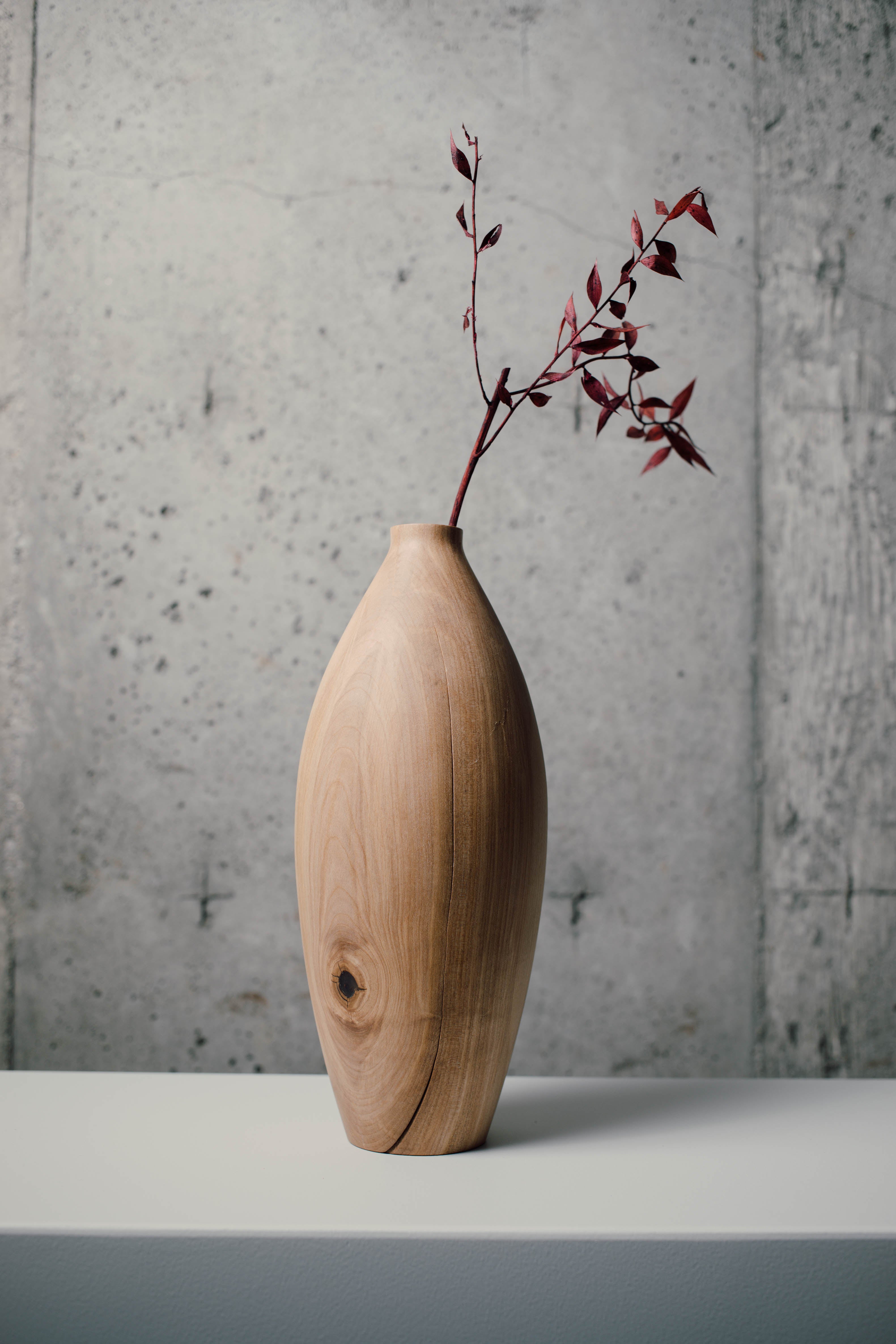 Smooth wooden vase with flowers against a concrete wall